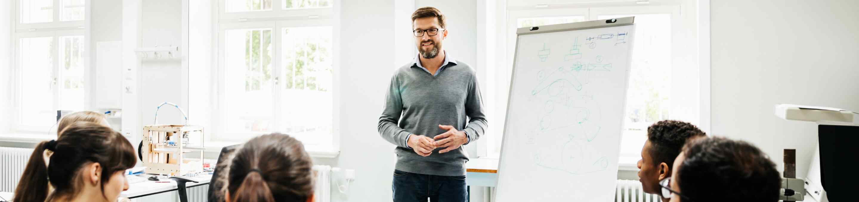 teacher in grey shirt lecturing in front of class