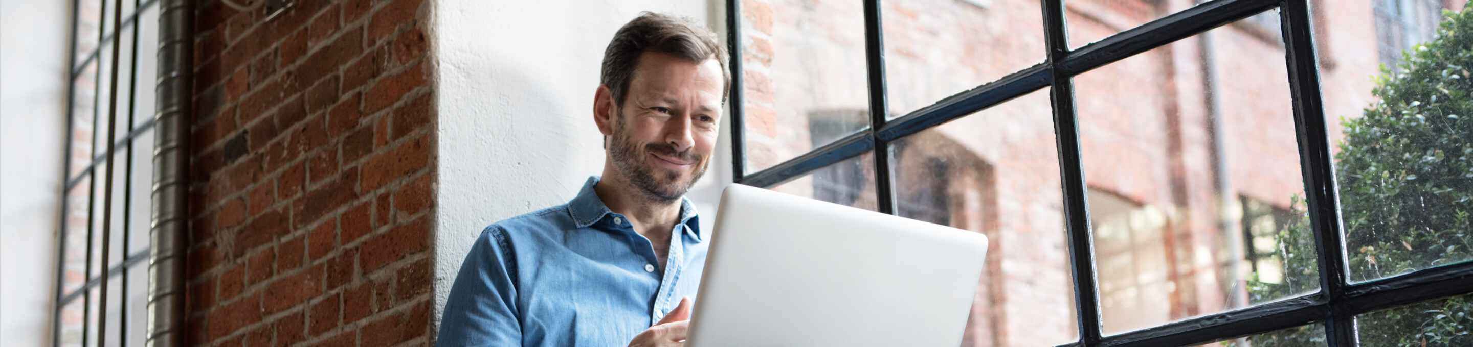 man using laptop in front of a red brick wall with windows